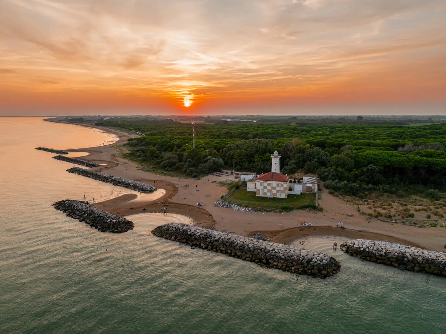 Tramonto sul mare con spiaggia e faro panoramico.