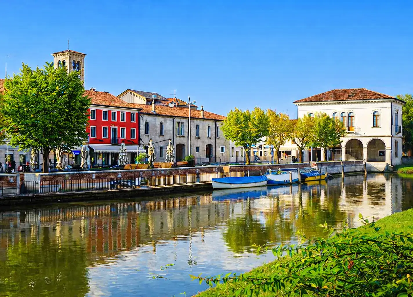 Canale con edifici colorati e barche, cielo sereno.