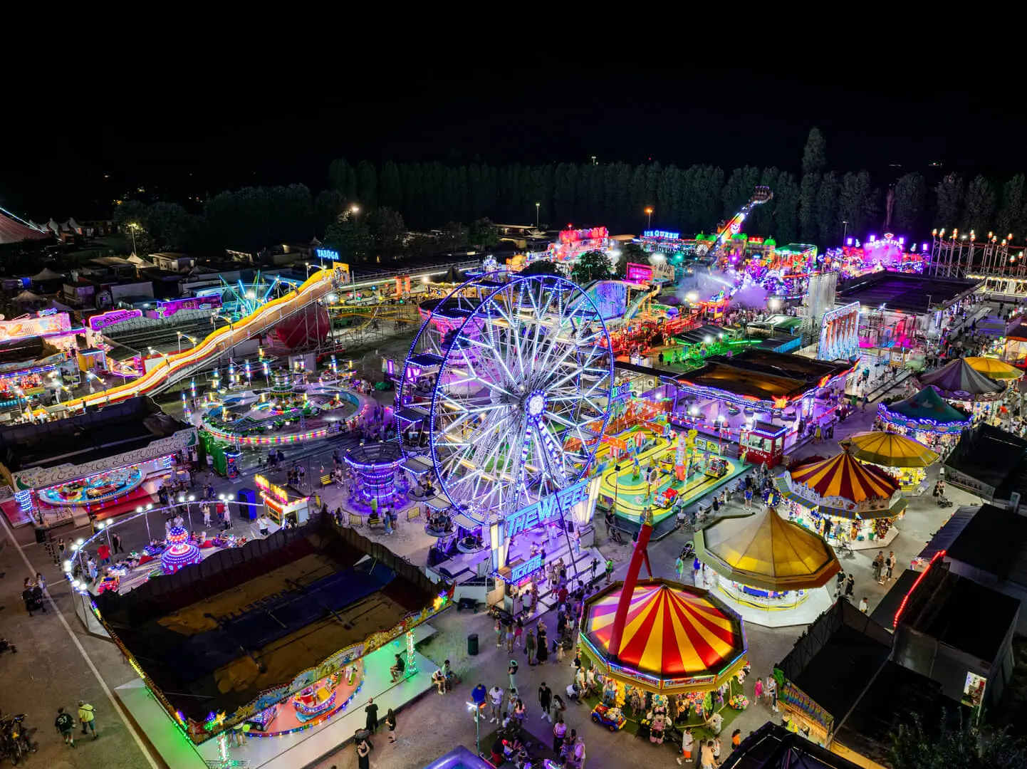 Luna park notturno con giostre illuminate e persone festanti.