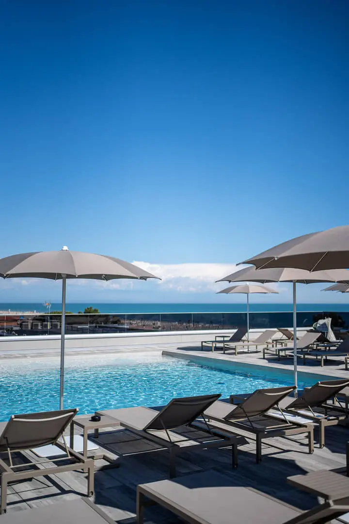 Piscina con lettini e ombrelloni vicino al mare.